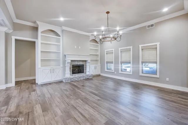 a view of an empty room with wooden floor fireplace and a window