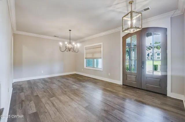 an empty room with wooden floor chandelier and windows