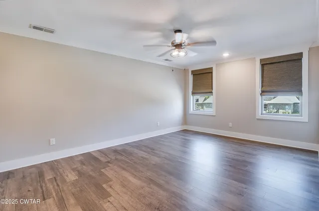 an empty room with wooden floor chandelier fan and windows