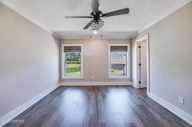 an empty room with wooden floor chandelier fan and windows