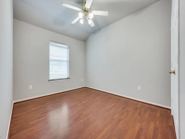 an empty room with wooden floor chandelier fan and windows