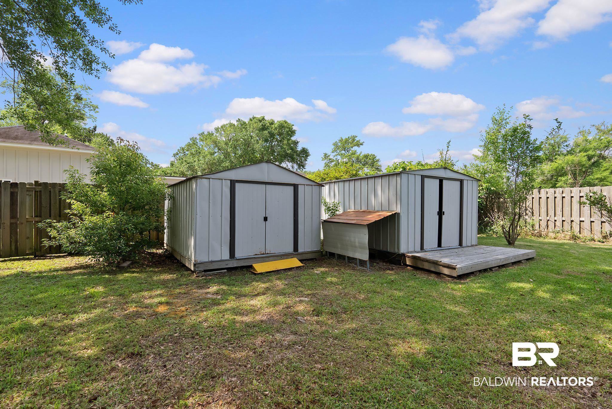 716 North Cedar Street Foley, AL 36535 - Photo 25 of 25 Expansive backyard featuring two metal storage sheds, a small animal enclosure, and a raised wooden platform