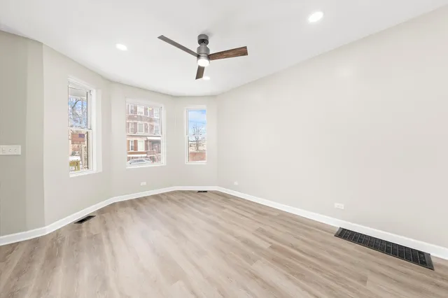 an empty room with wooden floor ceiling fan and windows