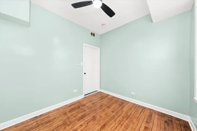 an empty room with wooden floor ceiling fan and window