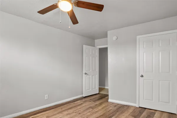 an empty room with wooden floor closet fan and windows