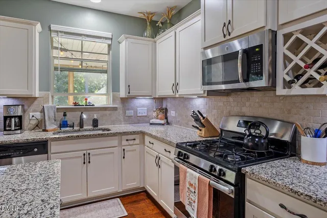 a kitchen with stainless steel appliances granite countertop white cabinets a window and a sink