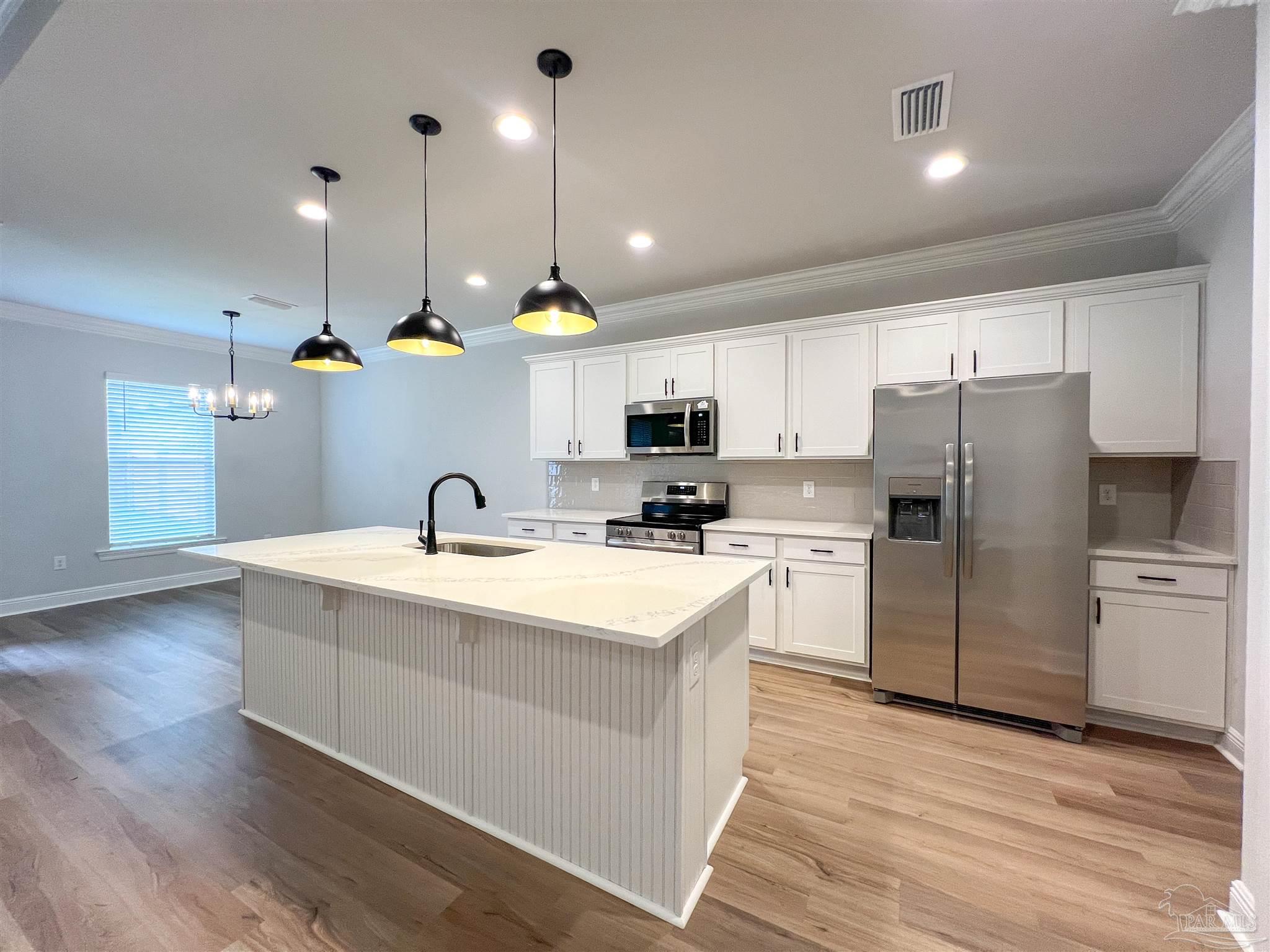 4605 Sago Palm Circle Milton, FL 32571 - Photo 3 of 33 a kitchen with kitchen island white cabinets stainless steel appliances and wooden floor