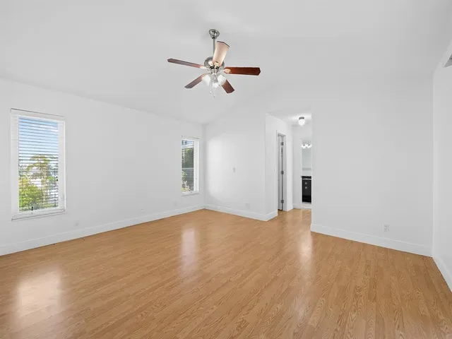 an empty room with wooden floor ceiling fan and windows