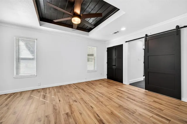 a view of an empty room with wooden floor and a ceiling fan