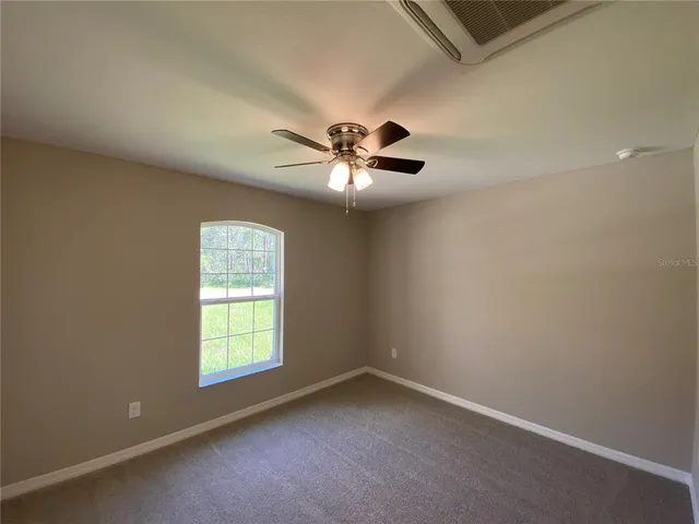an empty room with a chandelier fan and windows