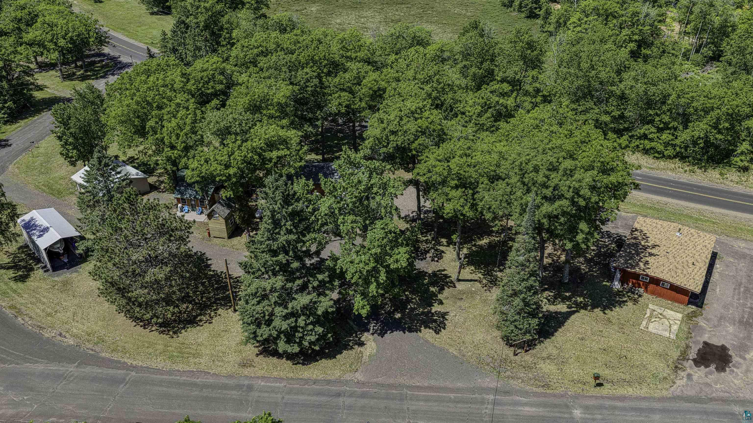 66075 Rooster Road Iron River, WI 54847 - Photo 7 of 52 Expansive property featuring mature trees, a red-sided structure with a light-colored roof, a gravel driveway, and additional structures