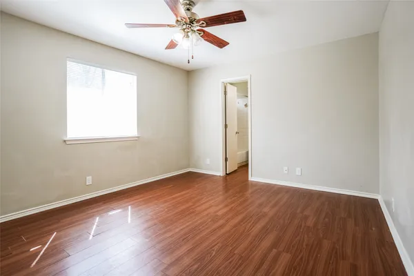 an empty room with wooden floor ceiling fan and windows