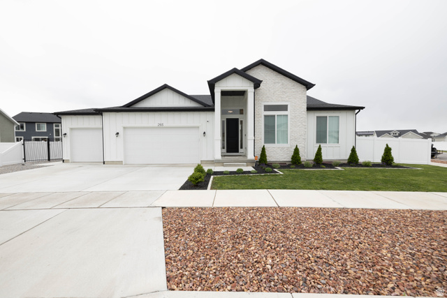 View of front of property with board and batten siding, a garage, concrete driveway, and a gate