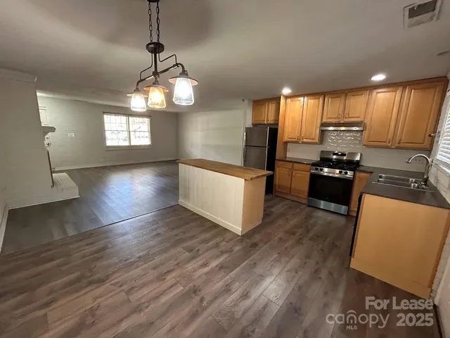 a kitchen with granite countertop wooden floors wooden cabinets and stainless steel appliances