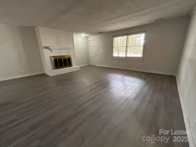 an empty room with wooden floor fireplace and windows