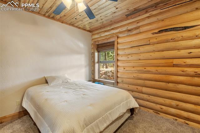 111 Blue Spruce Road Divide, CO 80814 - Photo 31 of 46 Bedroom featuring wood ceiling, rustic walls, carpet floors, and a ceiling fan
