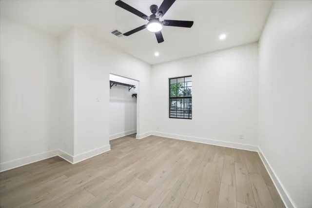 an empty room with wooden floor ceiling fan and windows