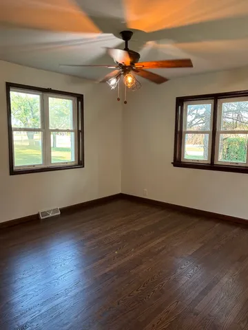 an empty room with wooden floor chandelier fan and windows