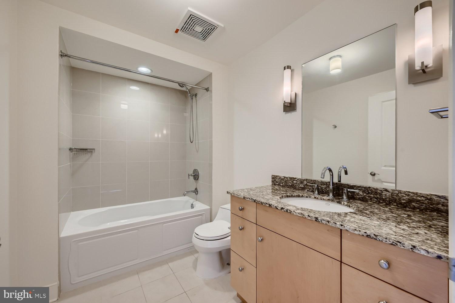675 President Street, Unit 1709 Baltimore, MD 21202 - Photo 11 of 33 a bathroom with a granite countertop sink a toilet a mirror a bathtub and shower