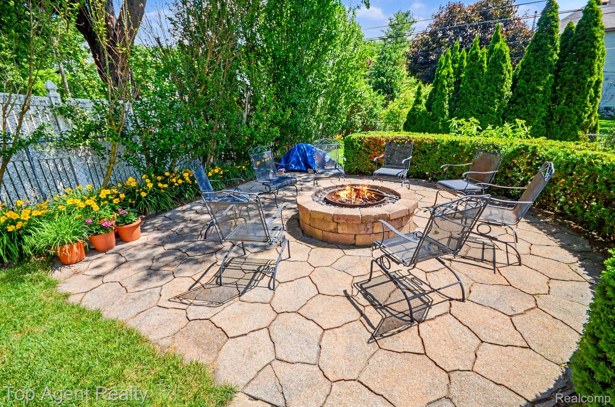 3759 Donley Avenue Rochester, MI 48309 - Photo 21 of 29 Flagstone patio with a built-in stone fire pit, surrounded by lush green landscaping, manicured hedges, and mature trees