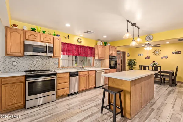 a kitchen with stainless steel appliances kitchen island granite countertop a stove top oven a sink dishwasher and white cabinets with wooden floor