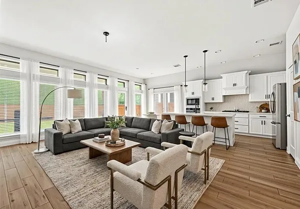 a living room with furniture kitchen view wooden floor and a large window