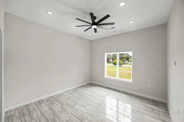an empty room with wooden floor a ceiling fan and windows