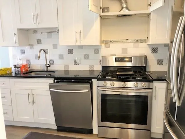 a kitchen with stainless steel appliances granite countertop a stove a sink and white cabinets