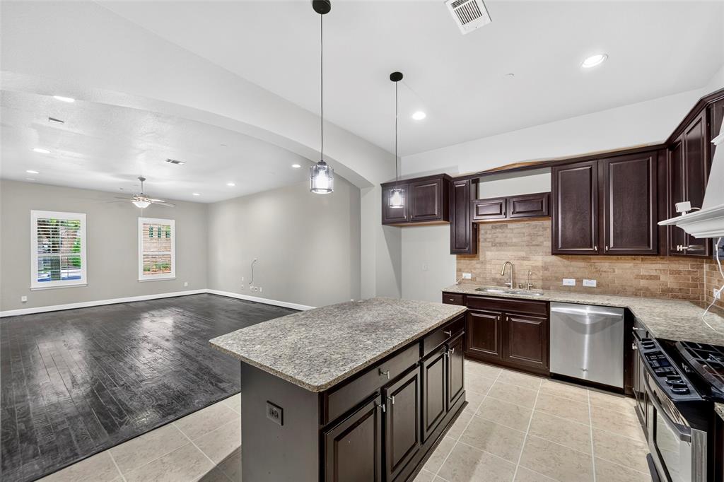 8607 Calvin Road Irving, TX 75063 - Photo 10 of 39 Open-concept kitchen featuring dark wood cabinetry, stainless steel appliances, and a central island with a stone-finish countertop