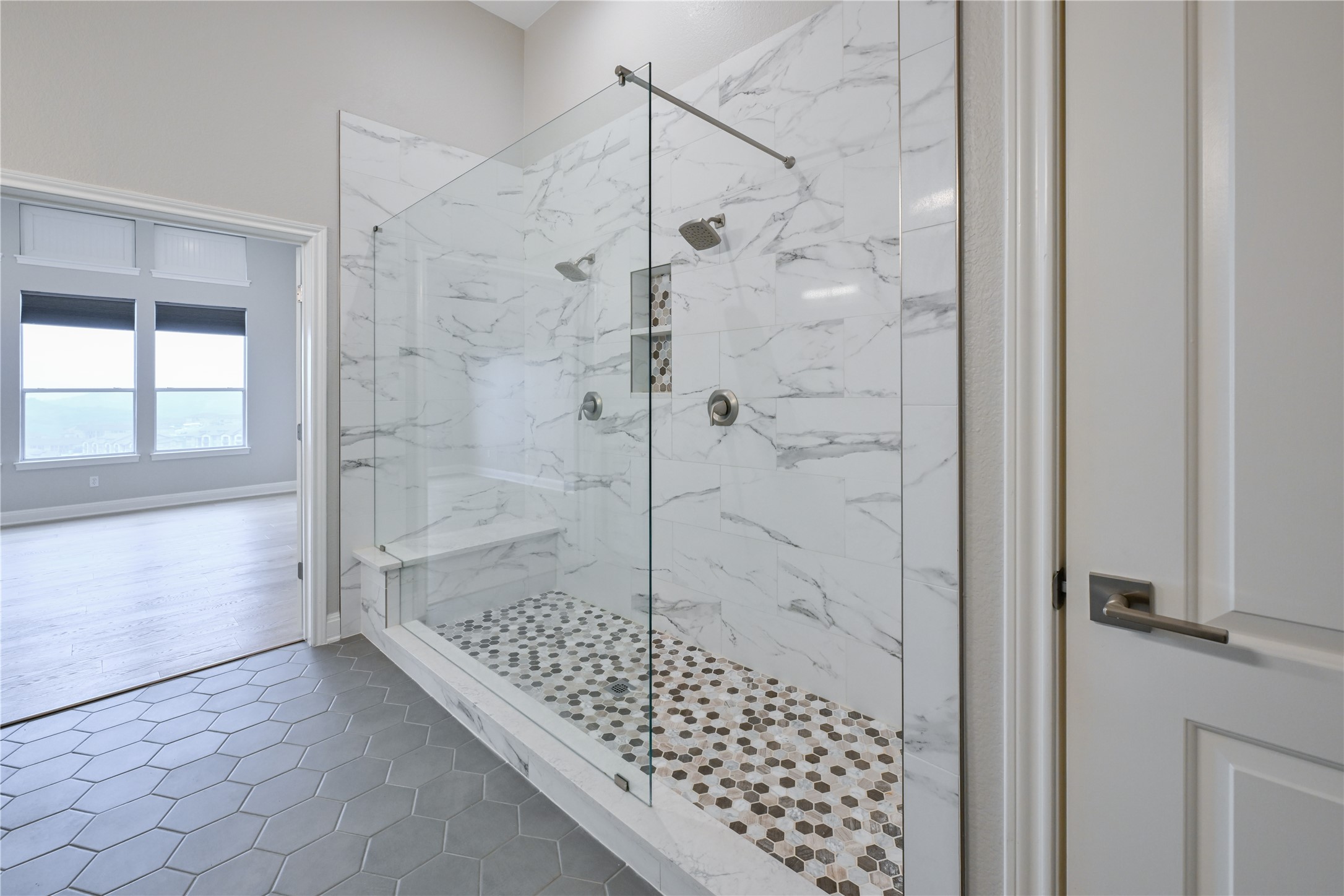 232 Sunrise Ridge Loop Austin, TX 78738 - Photo 19 of 37 Walk-in shower featuring clear glass enclosure, full-height marble-look tile, dual shower heads, integrated bench, and pebble-look floor