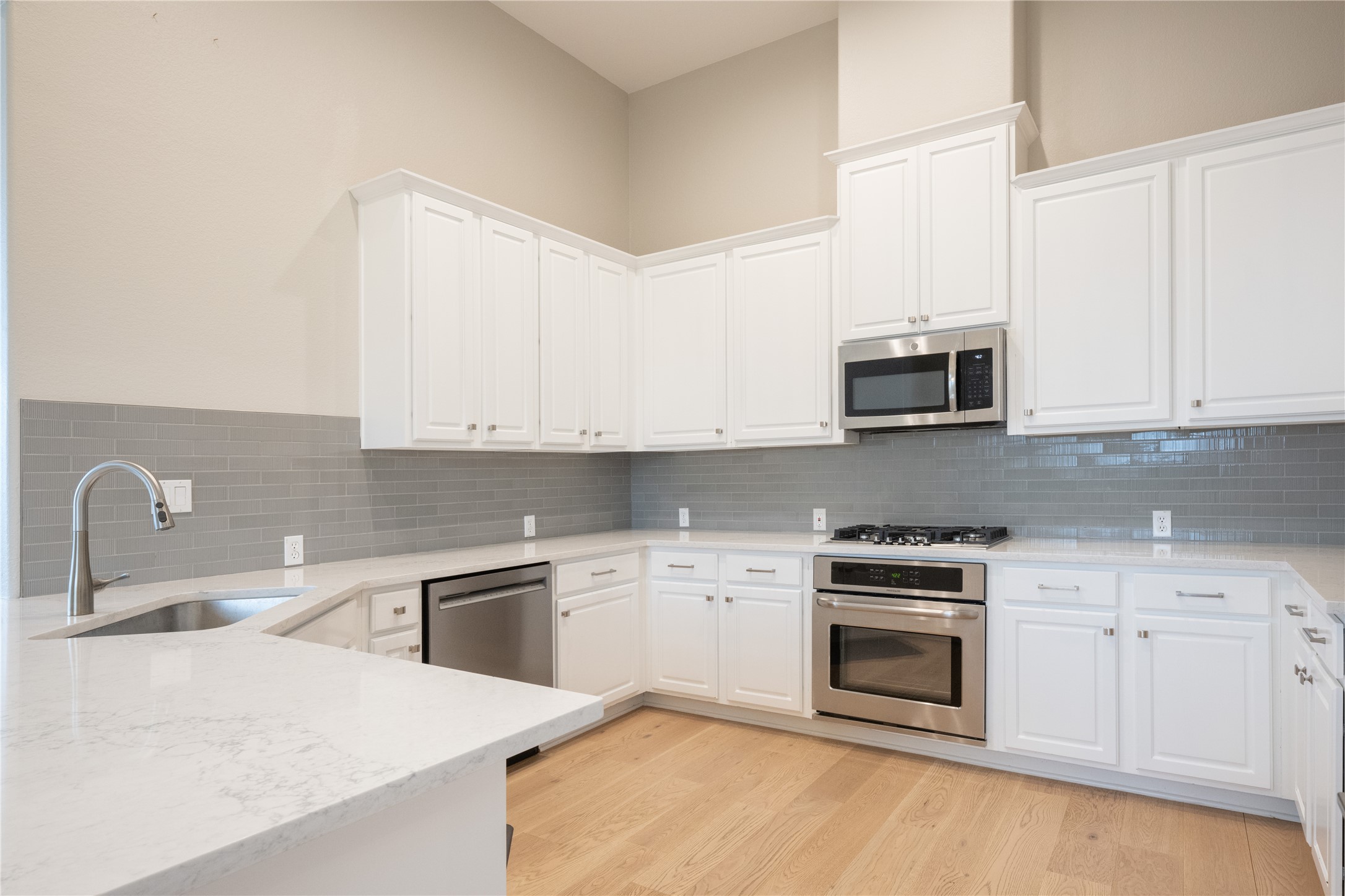 232 Sunrise Ridge Loop Austin, TX 78738 - Photo 10 of 37 Modern kitchen featuring white shaker cabinetry, stainless steel appliances, light-toned wood-finish flooring, and a gray subway tile backsplash