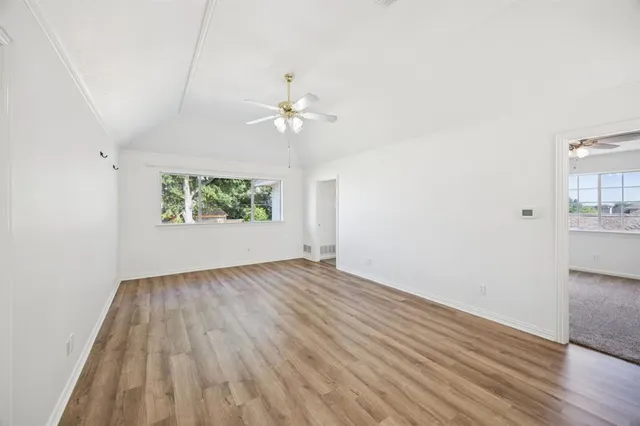 an empty room with wooden floor chandelier fan and windows