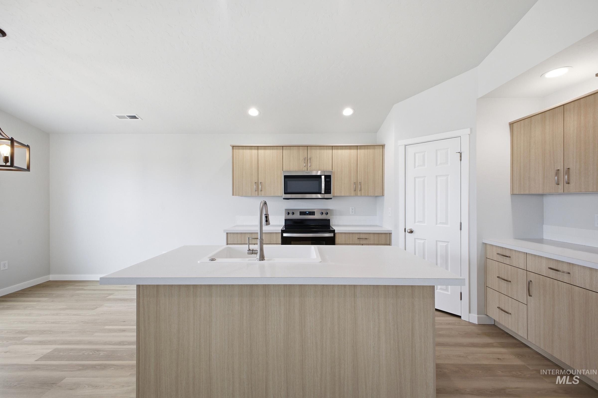 1598 Sunday River Street Middleton, ID 83644 - Photo 3 of 17 Open-concept kitchen featuring an island with an integrated sink, light wood-finish cabinetry, stainless steel appliances, white countertops, and wood-finish flooring