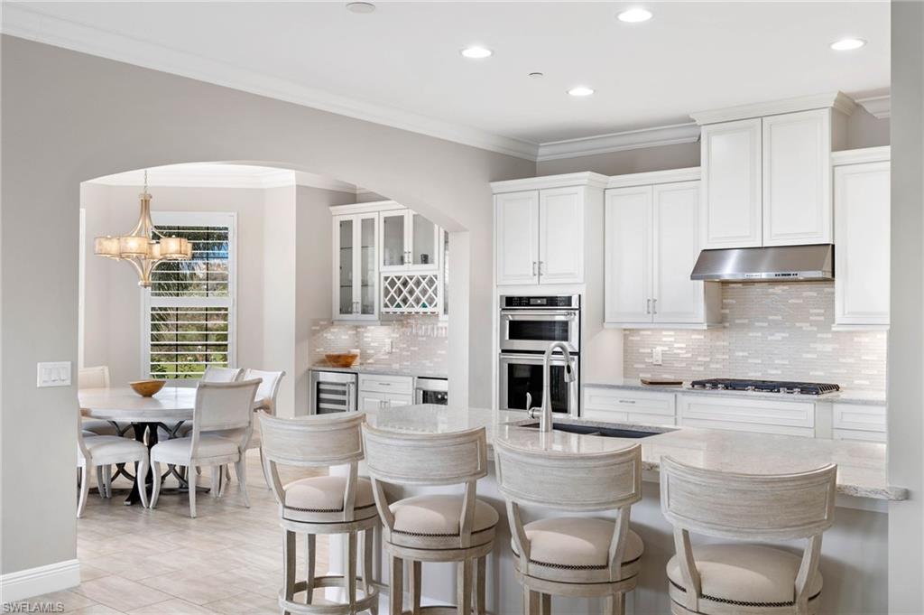 16449 Carrara Way, Unit 101 Naples, FL 34110 - Photo 11 of 35 Kitchen featuring crown molding, a breakfast bar, under cabinet lighting, appliances with stainless steel finishes, and wine cooler.
