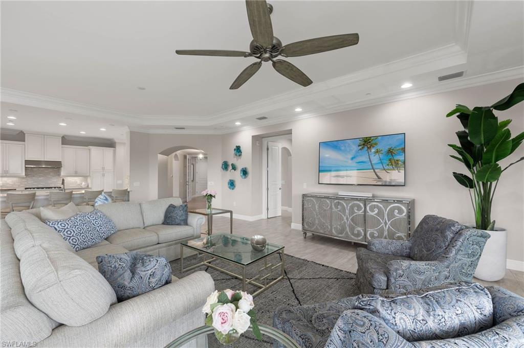 16449 Carrara Way, Unit 101 Naples, FL 34110 - Photo 5 of 35 Great Room featuring crown molding, a ceiling fan, a tray ceiling, and arched walkways.