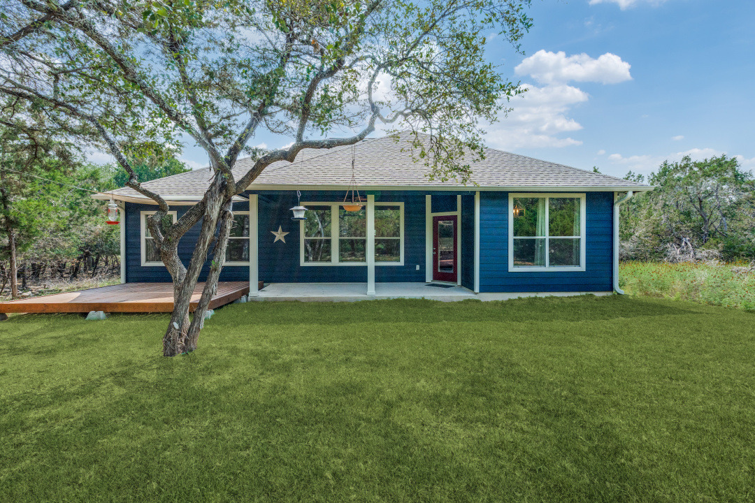 1848 Tanglewood Trail Spring Branch, TX 78070 - Photo 2 of 12 A classic blue siding home with a welcoming red door, complemented by a broad wooden deck and verdant lawn.