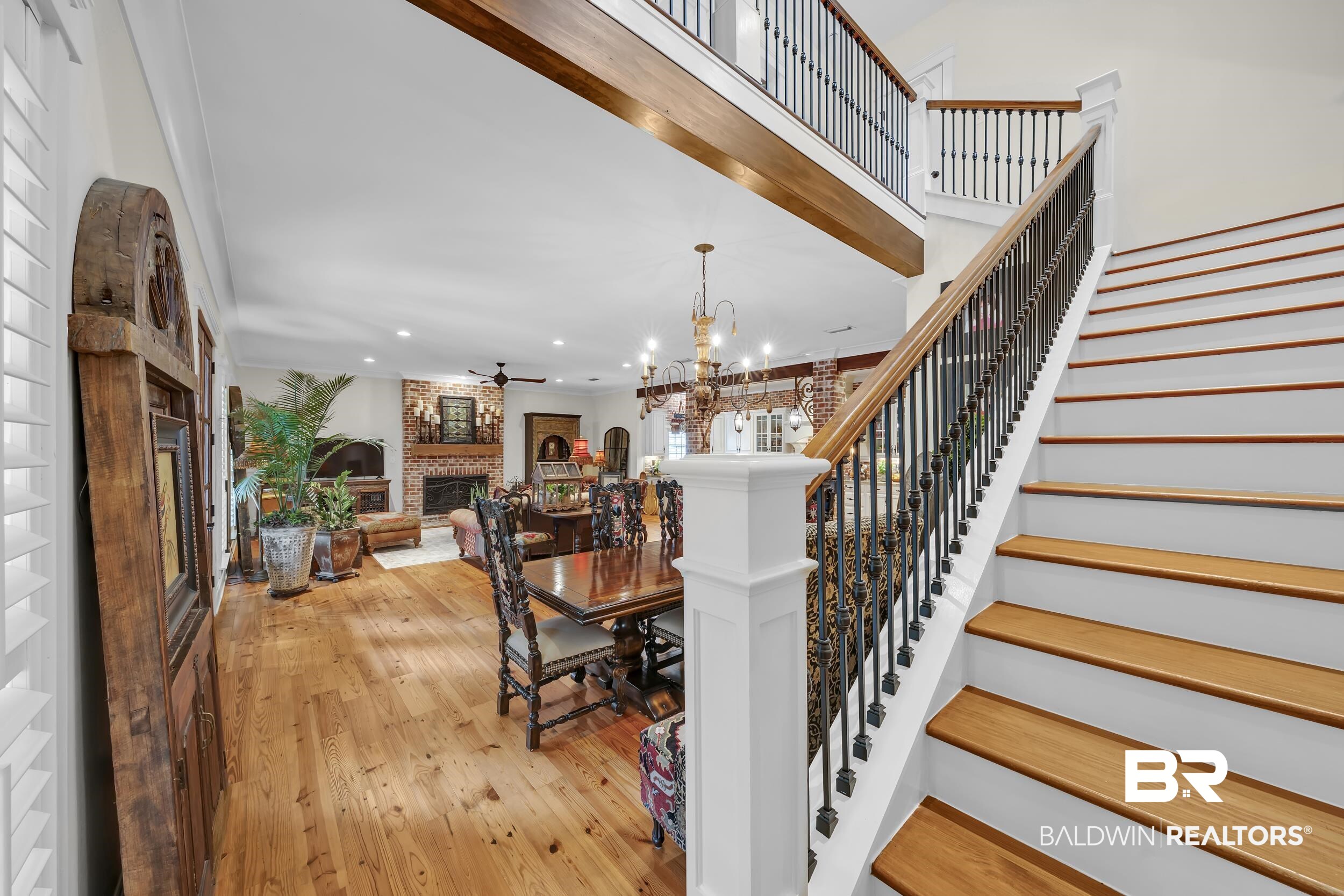12161 Jessamine Street Magnolia Springs, AL 36555 - Photo 3 of 70 Staircase featuring a brick fireplace, a ceiling fan, hardwood / wood-style floors, and a chandelier