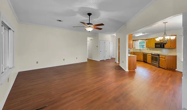 an empty room with wooden floor a ceiling fan and kitchen view