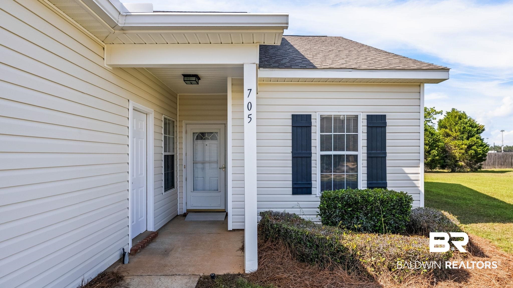 2651 South Juniper Street, Unit 705 Foley, AL 36535 - Photo 4 of 37 Exterior featuring light-colored siding, a covered entryway with house numbers, a white paneled front door with decorative glass, and a window with dark shutters