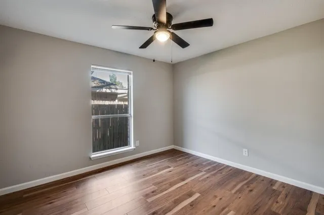 an empty room with wooden floor chandelier fan and windows