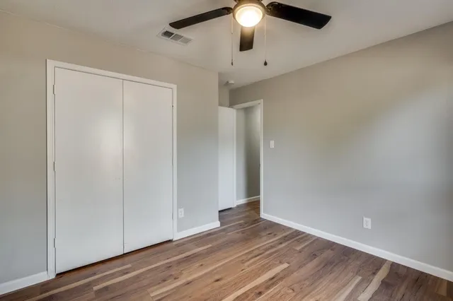 an empty room with wooden floor fan and windows