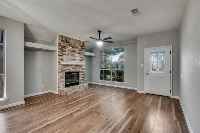 an empty room with wooden floor fireplace and windows