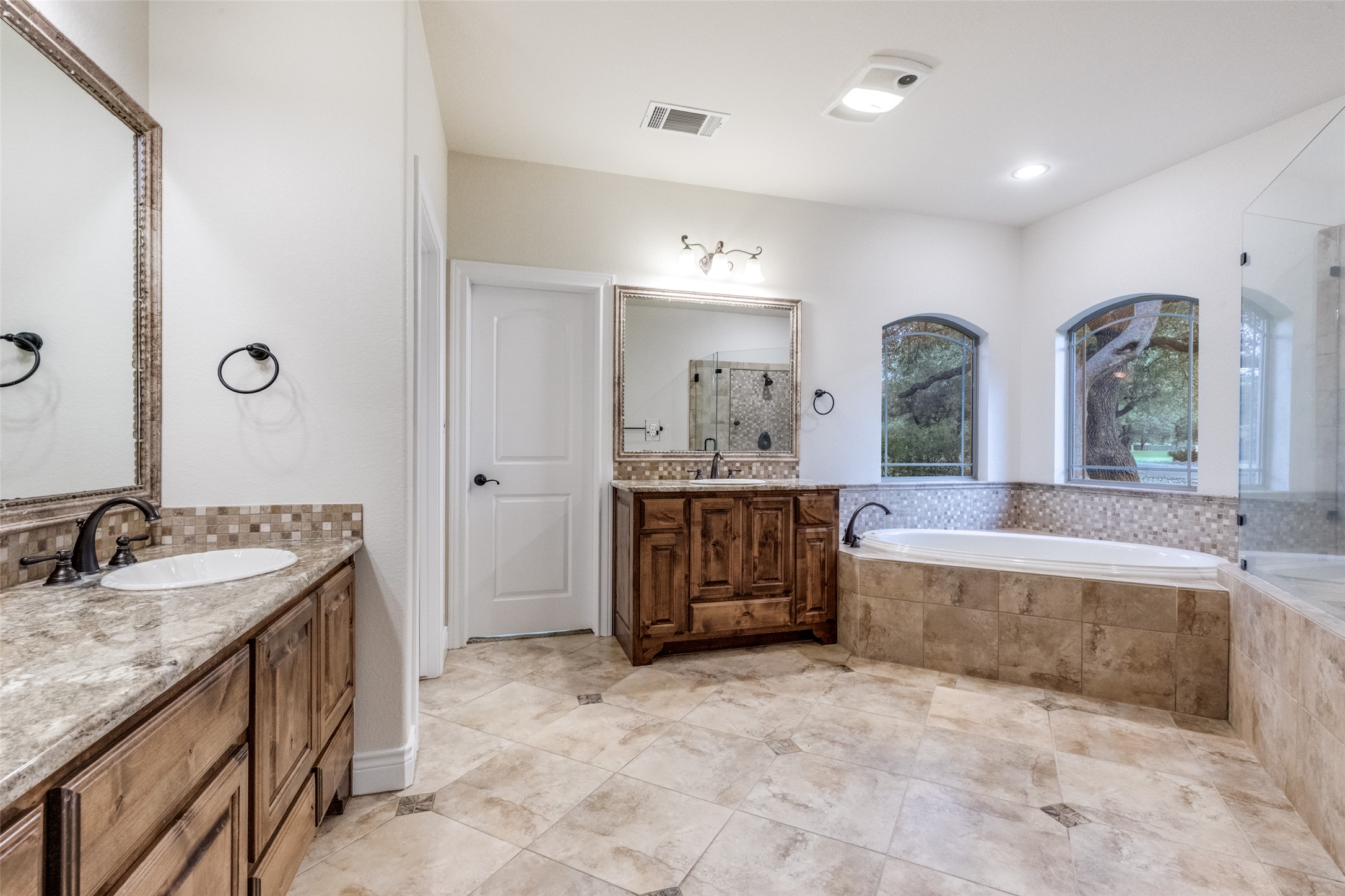101 Copper Leaf Court Georgetown, TX 78633 - Photo 15 of 31 Spacious bathroom featuring a built-in soaking tub, arched windows, dual vanity areas with stone countertops, and a glass-enclosed shower