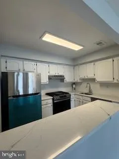 a kitchen with stainless steel appliances kitchen island granite countertop a refrigerator a sink dishwasher a stove with white cabinets and a refrigerator