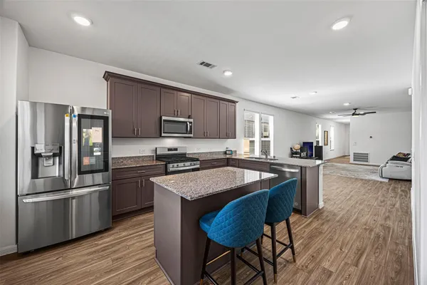 a kitchen with stainless steel appliances granite countertop a refrigerator a sink dishwasher a stove top oven a oven with wooden floors