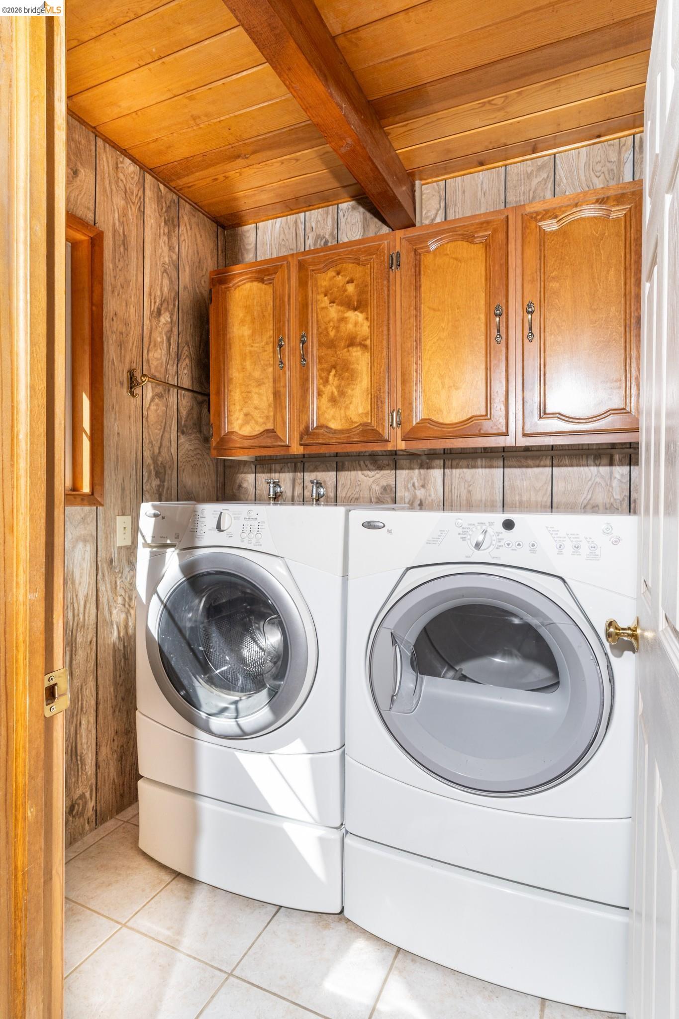 19390 Ferretti Road Groveland, CA 95321 - Photo 21 of 38 Laundry area featuring wood-paneled walls, wood beam ceiling, tile flooring, and integrated cabinetry