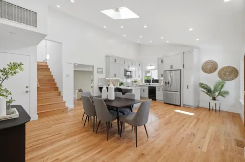 a kitchen with kitchen island white cabinets a refrigerator a stove a sink and a dining table with wooden floor