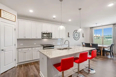 a kitchen with stainless steel appliances kitchen island granite countertop a stove a sink and white cabinets with wooden floor