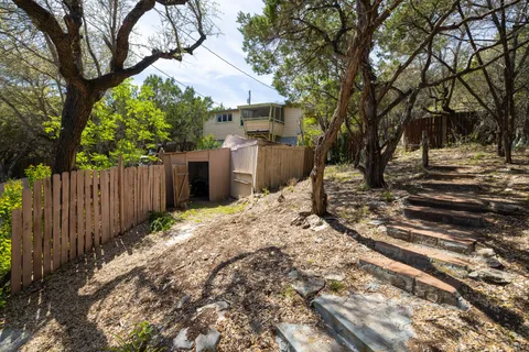 a view of a backyard with large trees and wooden fence
