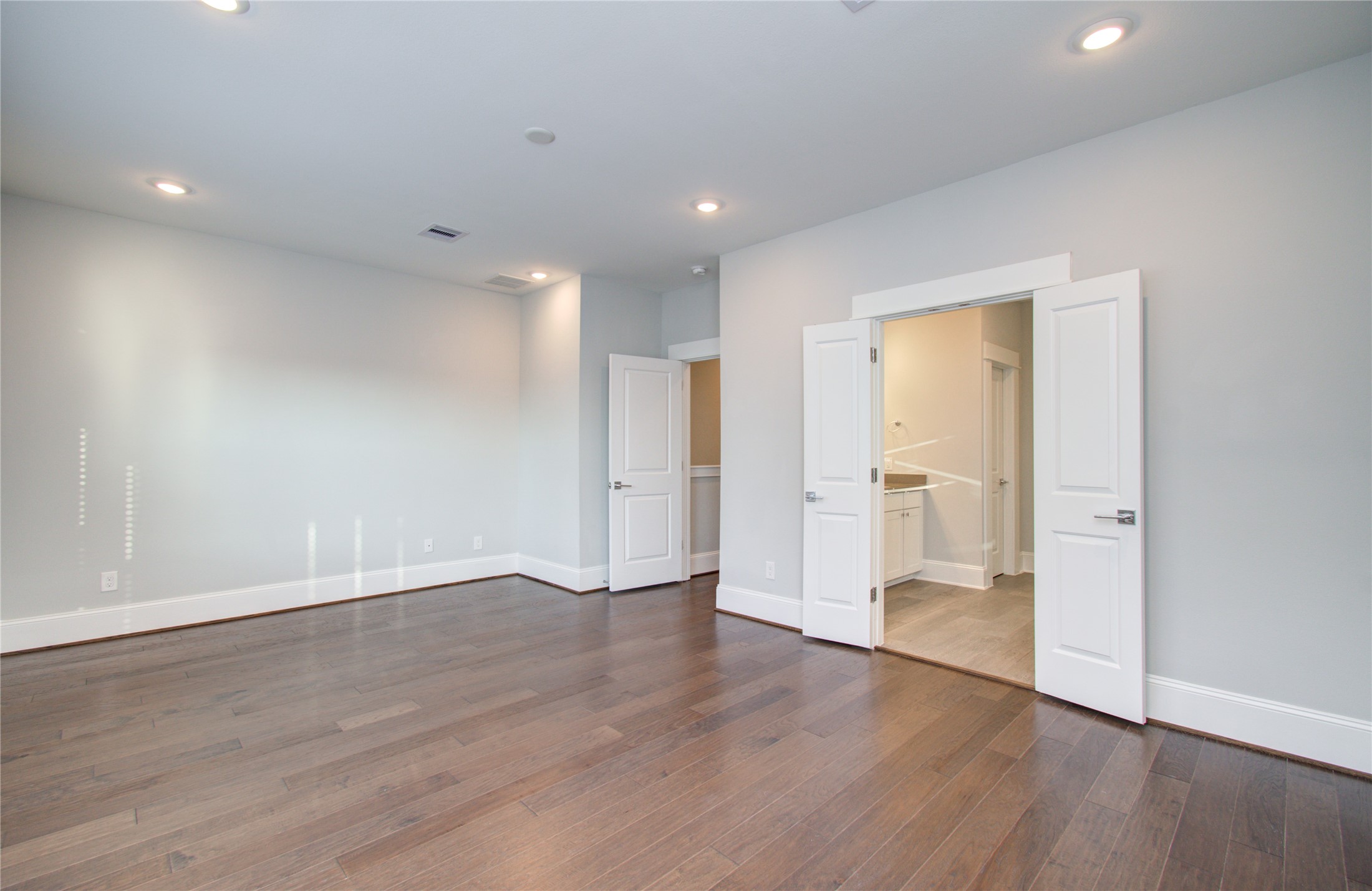 1262 North Post Oak Road, Unit A Houston, TX 77055 - Photo 34 of 50 The primary bedroom suite offers a spacious footprint with rich dark hardwood flooring and double doors leading into the en-suite bathroom. Recessed lighting brightens the open room.